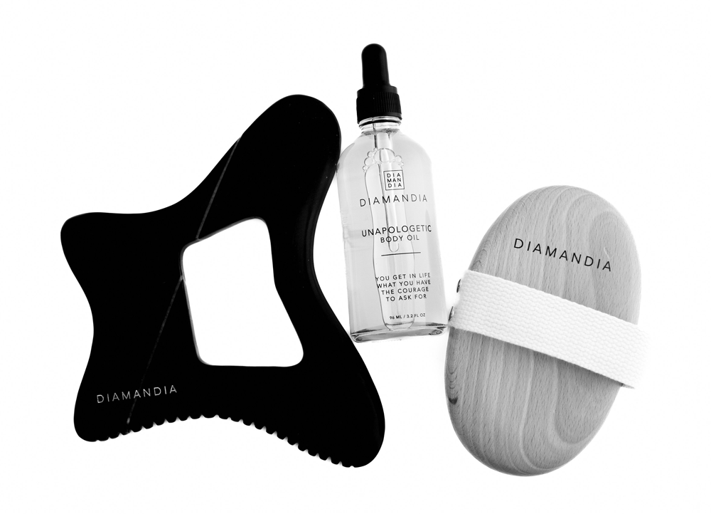 A serene spa setting with Bian stone Gua Sha tool, Unapologetic Body Oil, and a dry brush.