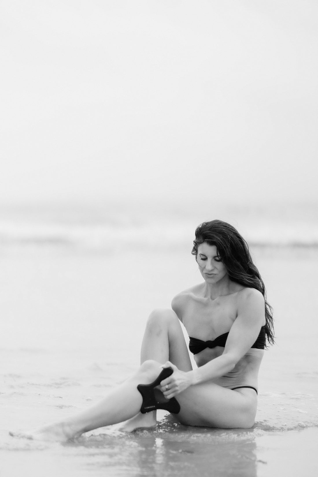A happy woman on the beach holding her Body Gua Sha tool made from Bian stone.